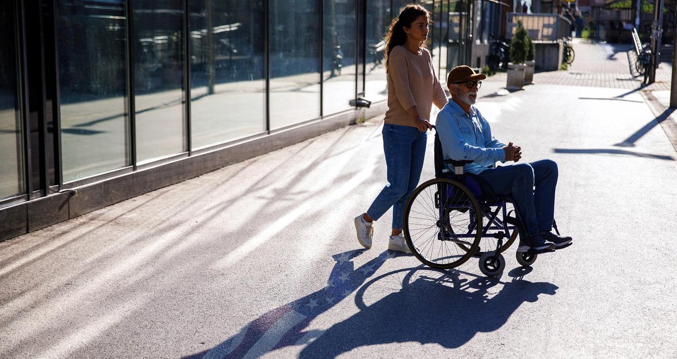 A woman pushing a man in a wheelchair outside, photo by Westend61 GmbH/Alamy Stock Photo